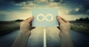 Two hands holding a piece of paper that has the infinity symbol on it. A road and clouds in the background