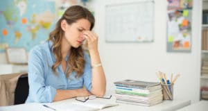 Stressed teacher sitting at a desk with her hand on her head