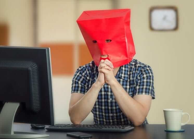 A male wearing a red paper bag over his head that has holes cut out for the eyes and mouth