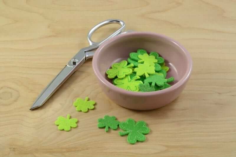 Scissors next to a bowl of four leaf clovers made out of green construction paper