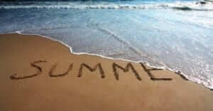 "Summer" written in the sand with a wave washing it away