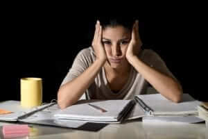Female sitting at a table with notebooks open and her head in her hands looking stressed