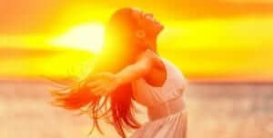 A woman with long, dark hair standing on the beach with her arms stretched out to her sides and the sunset behind her