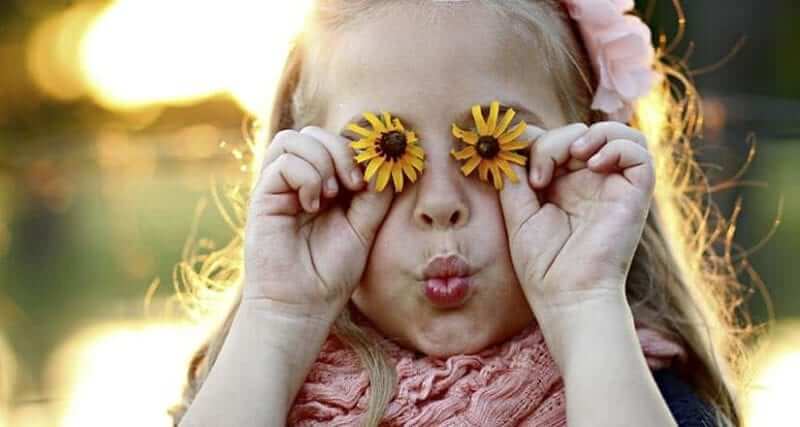 A little girl holding daisies in front of her eyes with her lips pursed