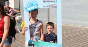 9 year old girl and 6 year old boy standing behind a teacher week at the beach window sign to get their picture taken