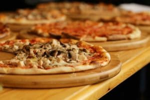 Pizza pies on round wooden trays, with a focus on one pie with toppings like mushroom and grilled chicken.