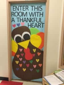 Classroom door that says "Enter this room with a thankful heart". There is a turkey with the students' names in hearts on it