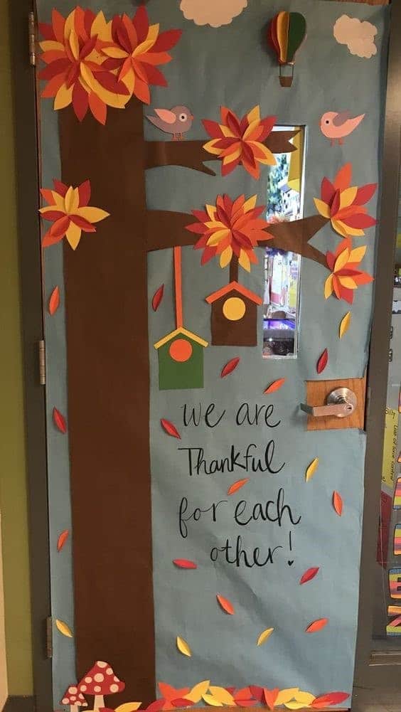 Classroom door that says "We are thankful for each other" with a tree, red/yellow/orange leaves, clouds in the sky, two bird houses and a couple of birds