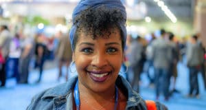 Head shot of female teacher wearing a jean jacket, lanyard, and silver hoop earrings with dark curly hair at NJEA convention