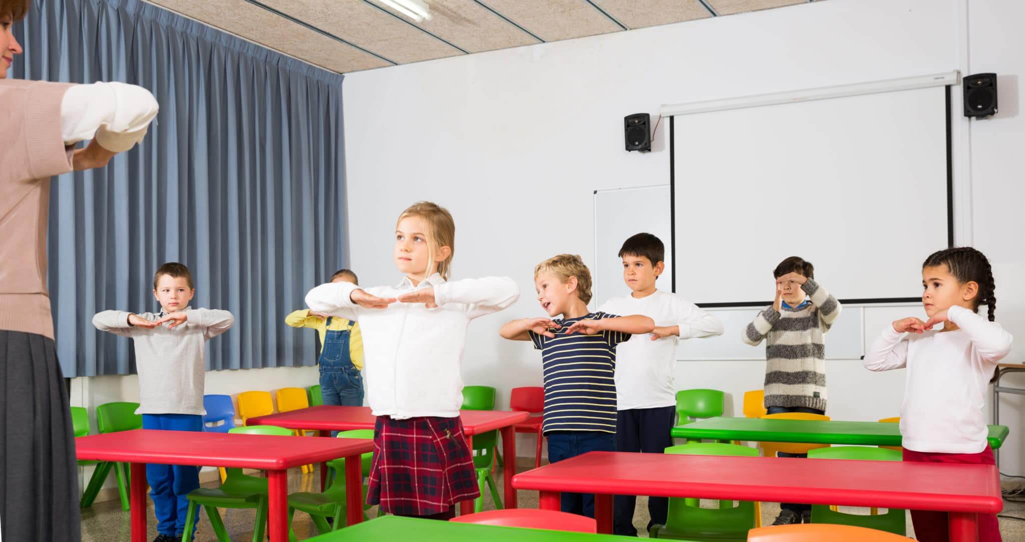 Elementary students standing in classroom doing arm stretches per the teacher's instructions
