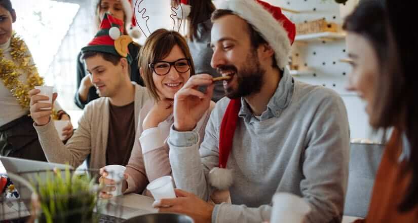 Teachers hanging out. One eating a cookie. Two holding white plastic cups. Two wearing Santa hats. One wearing reindeer ears.