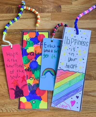 Colorful bookmarks made by children that have a string of beads attached. One says "hope is the heartbeat of the soul" and another says "happiness is in your heart" with a rainbow, hearts, and stars