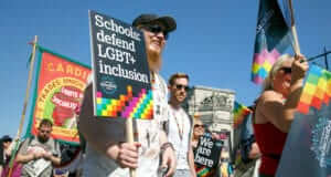 Participants marching for LGBT+, one holding a sign that says "Schools defend LGBT+ inclusion"