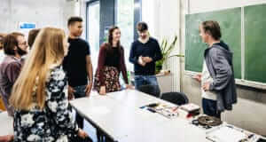Young adults standing around a table in a classroom with a chalkboard