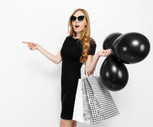 A woman holding balloons and shopping bags and pointing at other stores that have teacher discounts