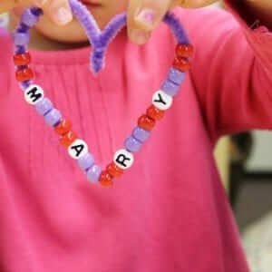 A child holding a necklace made out of beads that spells out the name Mary