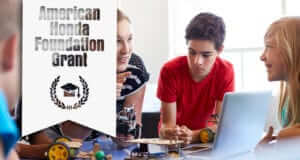 Female teacher and students leaning over a desk that has a laptop and parts to build a remote control car