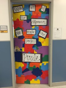 A classroom door decorated with multi-colored puzzle pieces and says "With all of our differences we make the perfect puzzle". Sign next to door says Ms. Marshall, Fourth Grade, 228