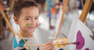 A little boy smiling and painting on an easel