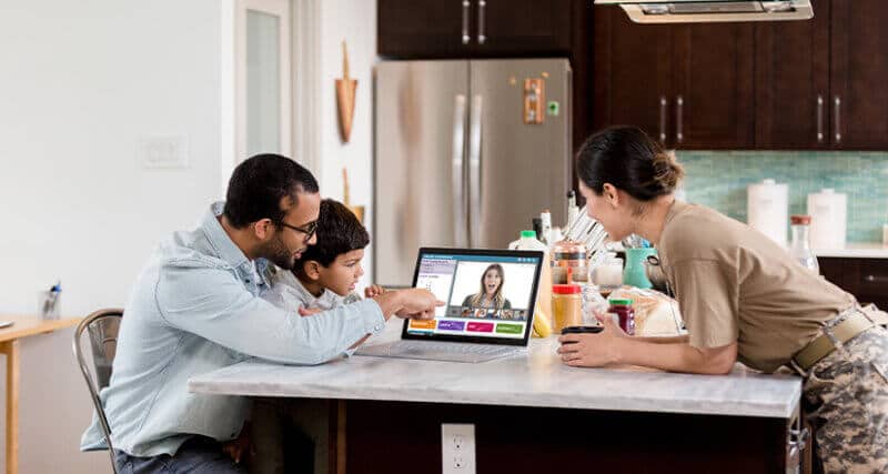 A young students and his parents in the kitchen on a laptop video conferencing with the teacher