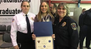 Renee Hollingsworth holding a certificate with her sister standing on her left and her mom stand on her right. All 3 are EMT's