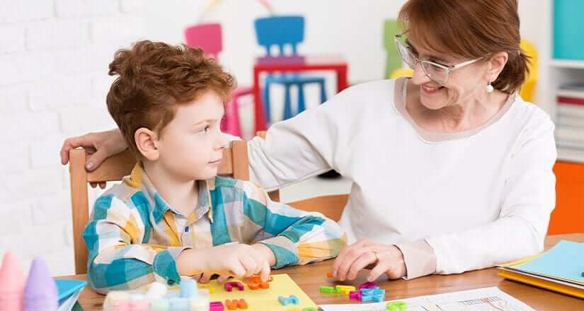 Young student sitting at desk with teacher playing with alphabet puzzle game