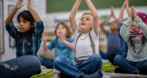 Young children sitting on the floor of a classroom doing yoga poses