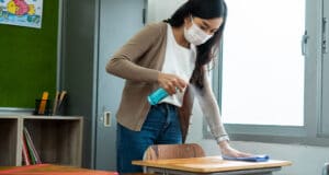 Female teacher sanitizing a desk in a classroom