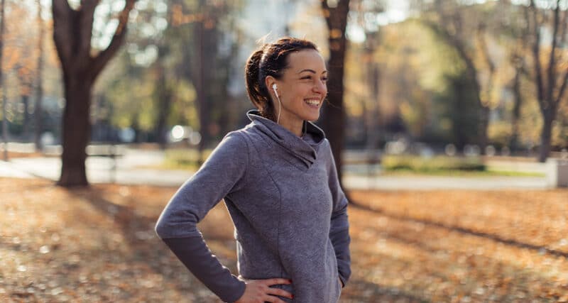 Female standing outdoors with her hands on her hips wearing workout attire and wireless headphones