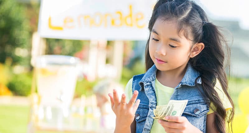 Little girl counting money at a lemonade stand
